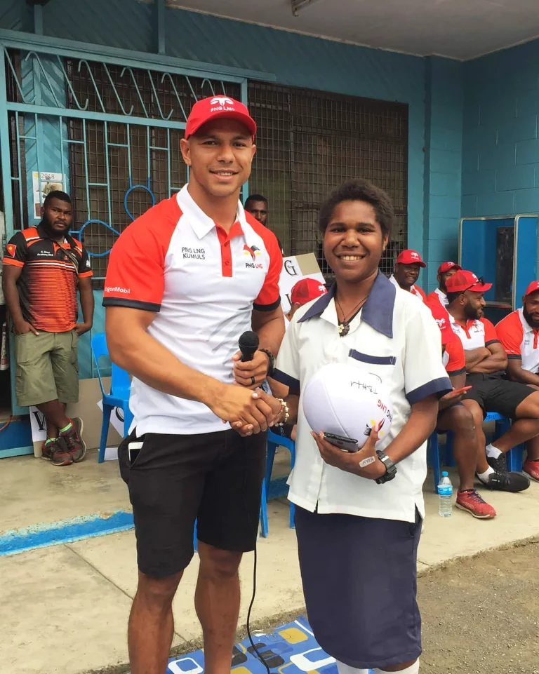 David Mead smiling shaking hand of student while doing community work with PNG Kumuls