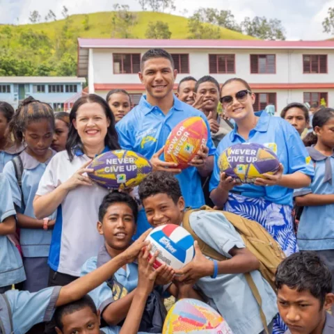 David Mead with wife Taneal Mead and Grass Skirt Project's Bronwyn Wright holding footballs and smiling with school children in Papua New Guinea